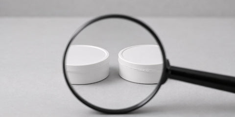 Magnifying glass checking two nicotine pouch cans for signs of counterfeiting