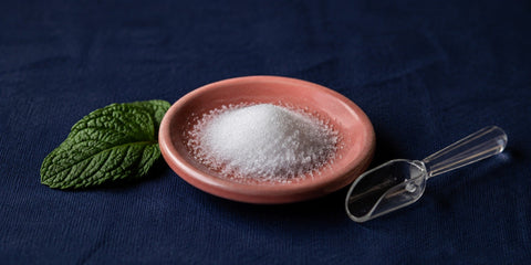 Sweetener crystals in a dish beside a mint leaf