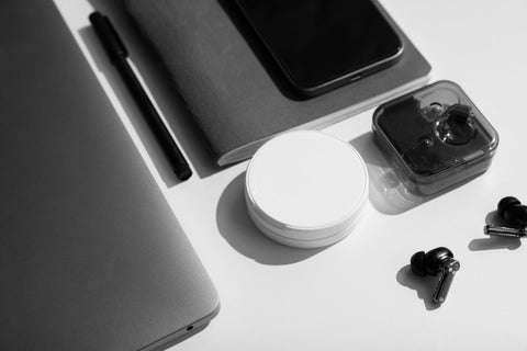 White nicotine pouch can on a desk with earbuds, a notebook and a laptop