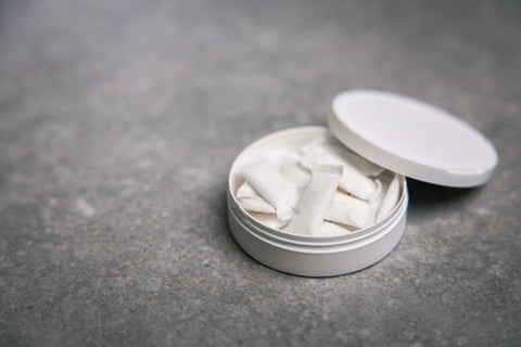 Open white can of nicotine pouches on a grey surface