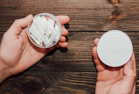 Hands holding an open can of white nicotine pouches and its lid