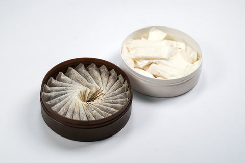 Open can of portion snus next to an open can of white nicotine pouches
