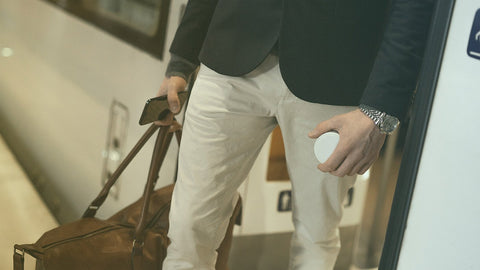 Adult traveller holding a white nicotine pouch can and a bag on a train platform