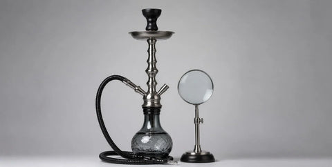 Shisha water pipe beside a magnifying glass on a grey background